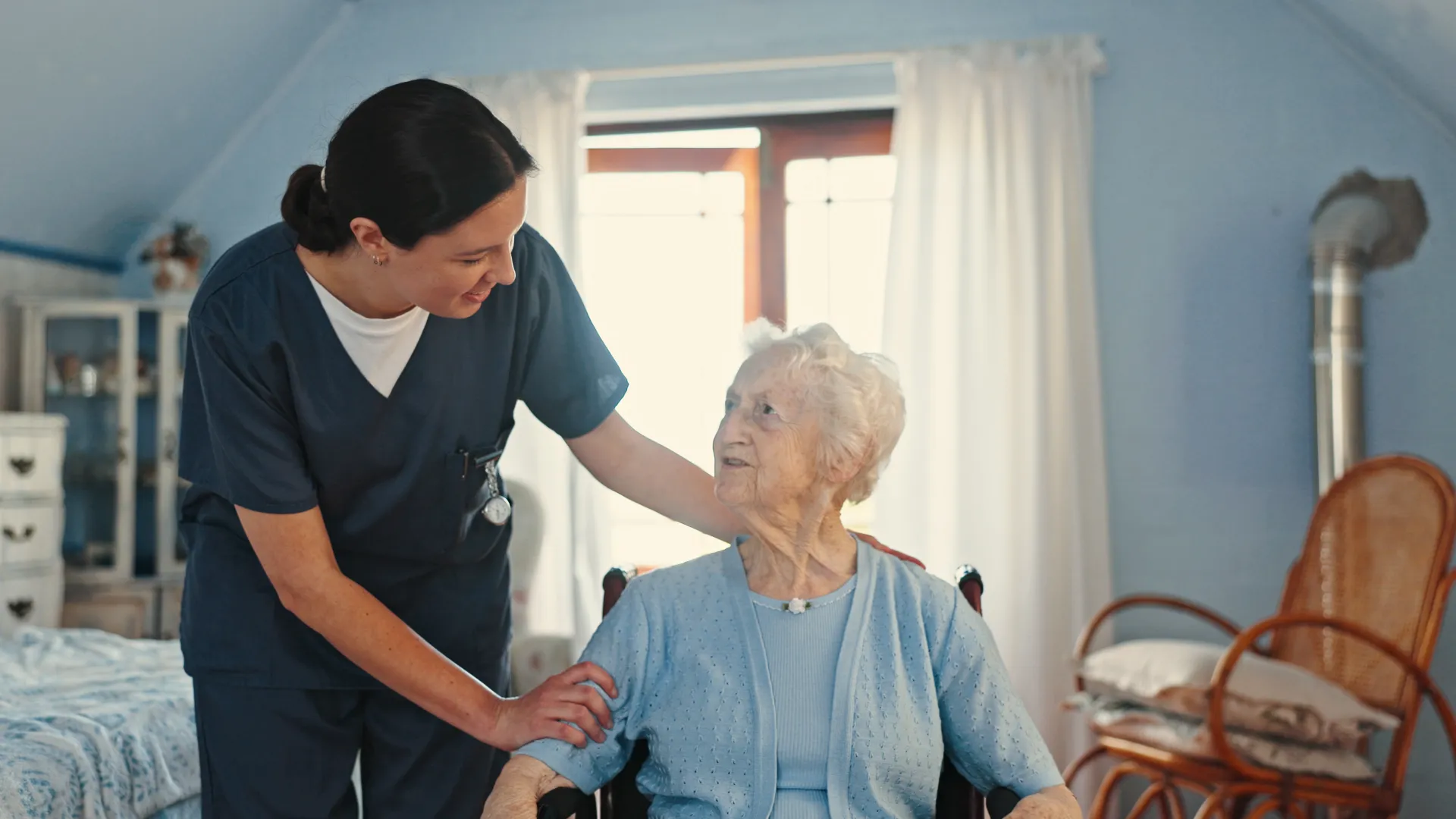 Caregiver interacting warmly with elderly woman in a bright, cozy room.