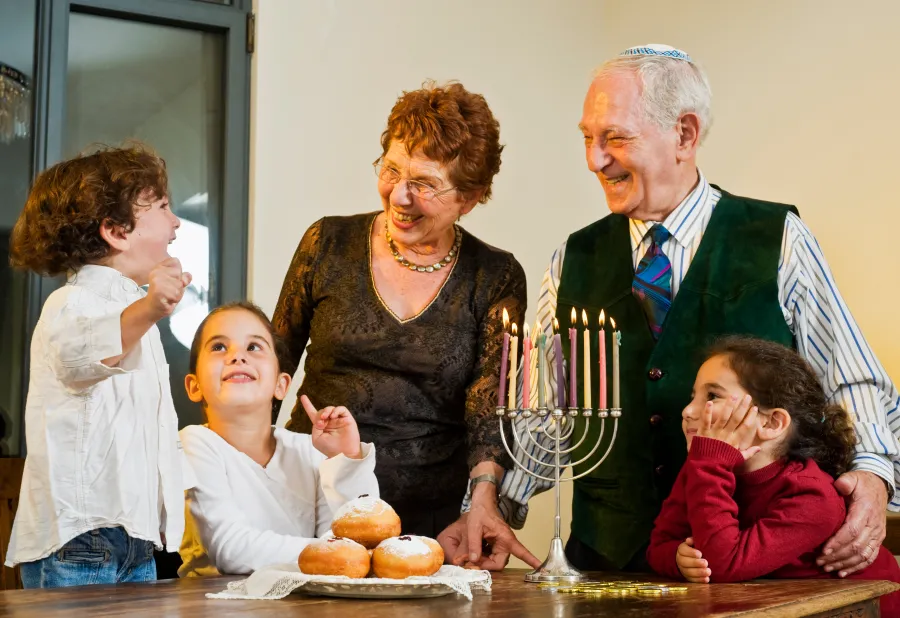 A joyful family celebrating Hanukkah with children, menorah, and traditional donuts on a table.