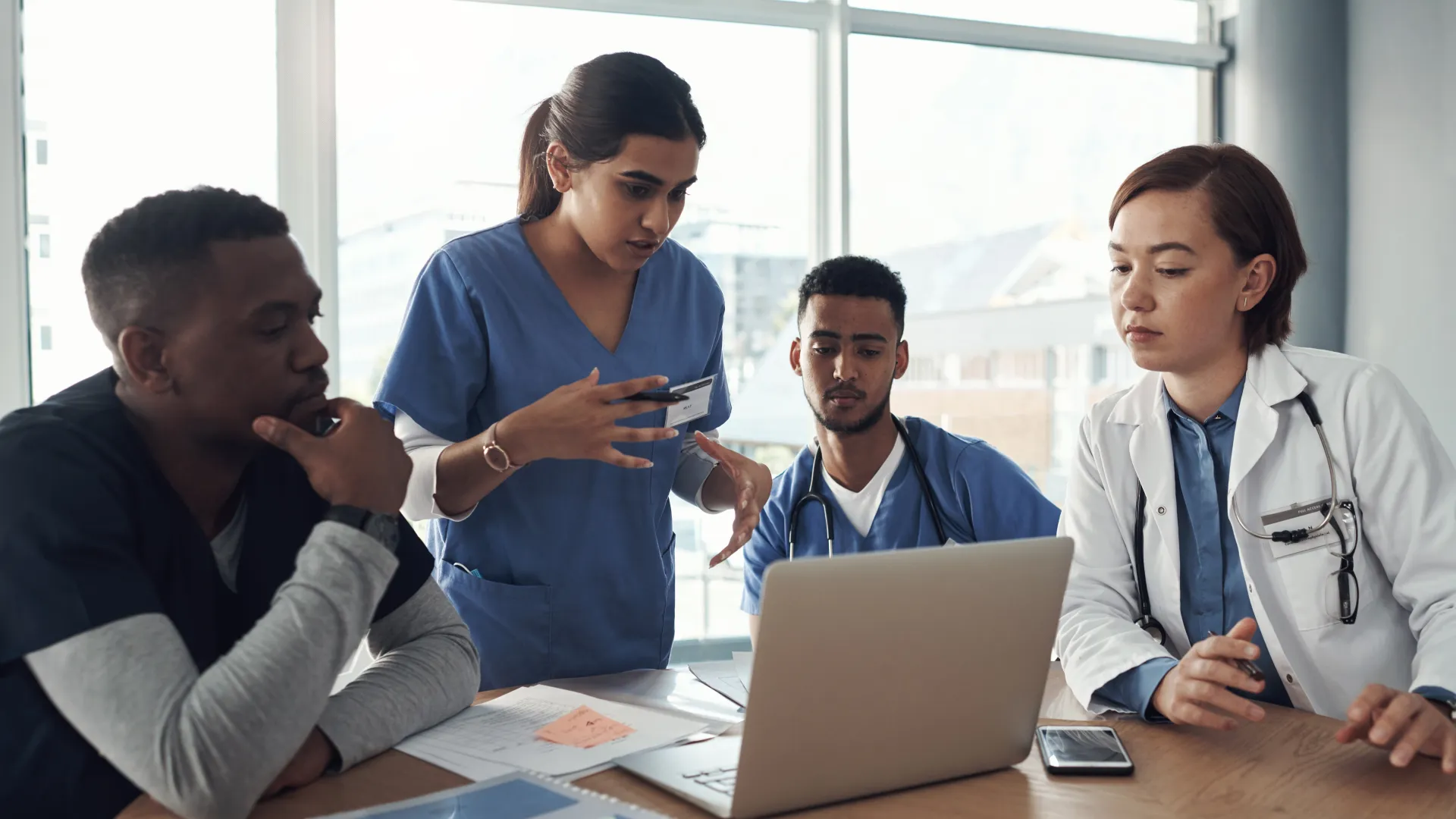 Four medical professionals collaborating around a laptop in a modern workspace.