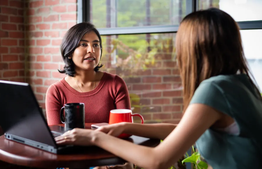 a couple of women sitting at a table looking at a laptop