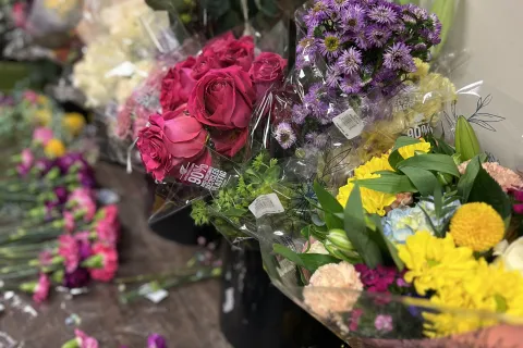 Assorted colorful fresh flower bouquets including pink roses, purple asters, and yellow blooms arranged on a wooden table.