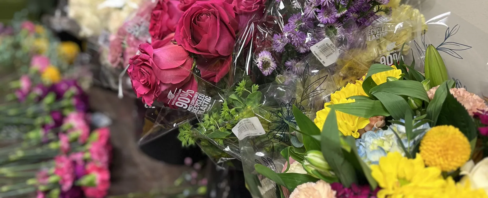 Assorted colorful fresh flower bouquets including pink roses, purple asters, and yellow blooms arranged on a wooden table.