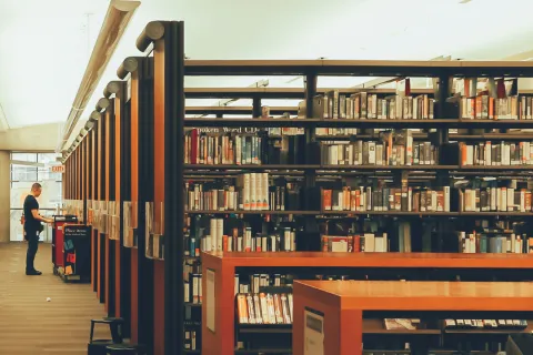 Spacious modern library aisle with bookshelves filled with books and a person browsing at the end.