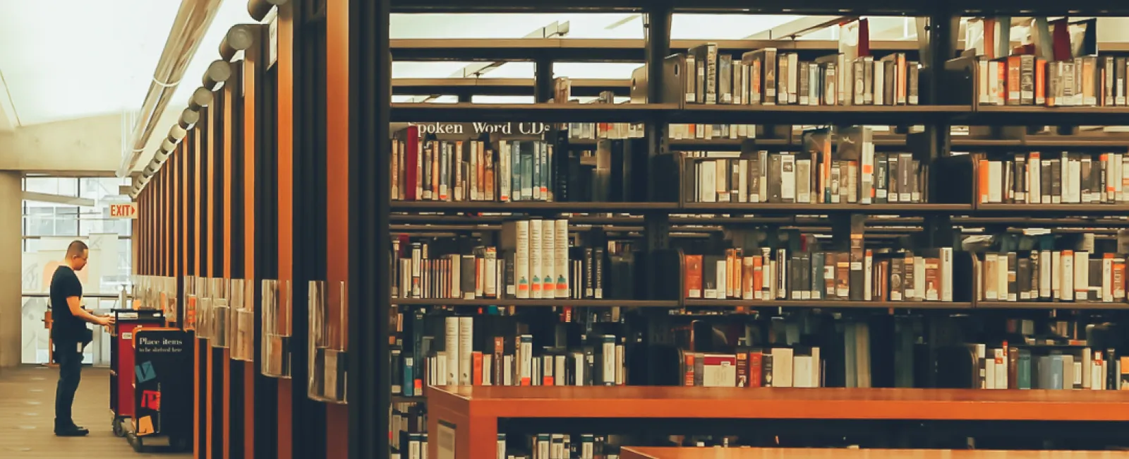 Spacious modern library aisle with bookshelves filled with books and a person browsing at the end.